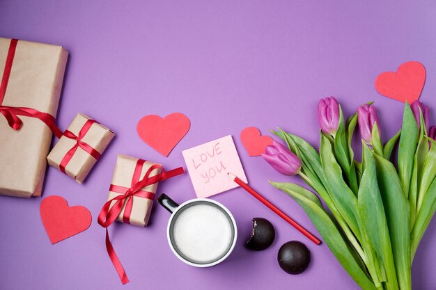 Valentine Hintergrund mit Geschenkbox süße Herzen und Tulpen auf violettem Tisch Draufsicht flach liegen