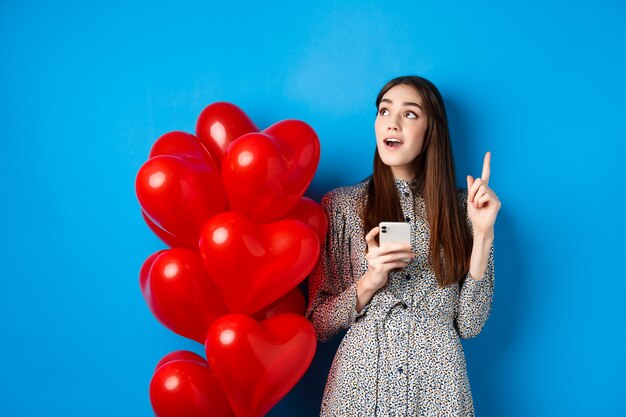 Valentinstag-Bild eines romantischen Mädchens, das eine Idee vorbringt, nachdem es das Handy benutzt hat, das den Finger nach oben hebt ...
