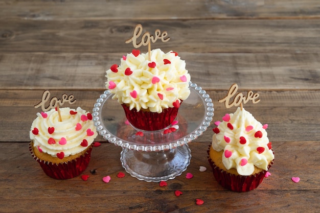 Valentinstag. drei cupcakes mit roter topping-dekoration und holzschild mit dem wort love auf holzhintergrund. platz kopieren.