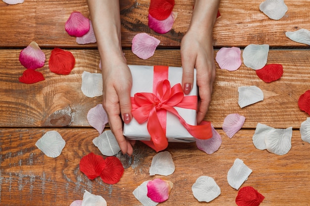 Valentinstag Geschenk und weibliche Hände auf Holz mit Blütenblättern