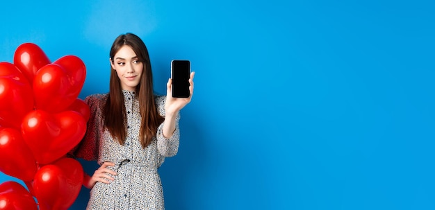 Kostenloses Foto valentinstag hübsche lächelnde frau im kleid, das leeren smartphone-bildschirm zeigt, der nahe romantisch steht