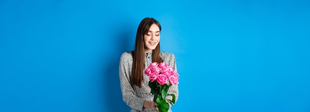 Valentinstag-Konzept Romantisches Mädchen im Kleid, das Blumen glücklich anschaut und den Strauß rosa ro anlächelt