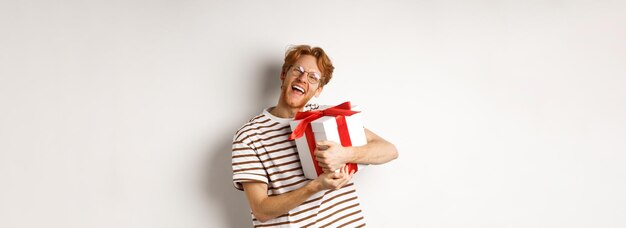 Valentinstag- und Feiertagskonzept Glücklicher rothaariger Mann, der seine Geschenkbox umarmt und sich mit Blick auf c bedankt