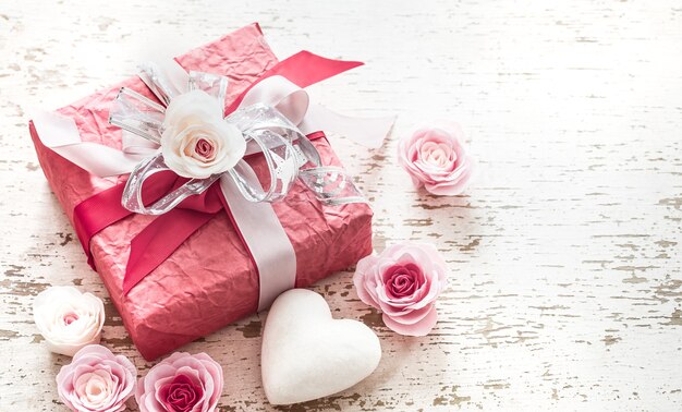 Valentinstag- und Muttertagskonzept, rote Geschenkbox mit Schleife und Rosen auf hellem hölzernem Hintergrund