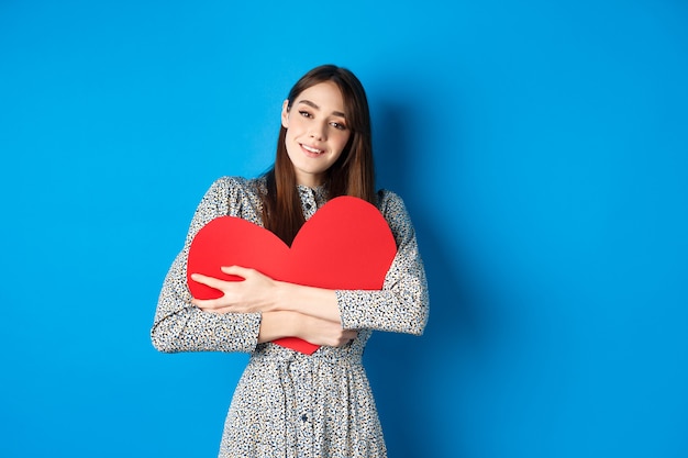 Valentinstag verträumte romantische frau, die großen roten herzausschnitt umarmt und sinnlich in die kamera schaut...