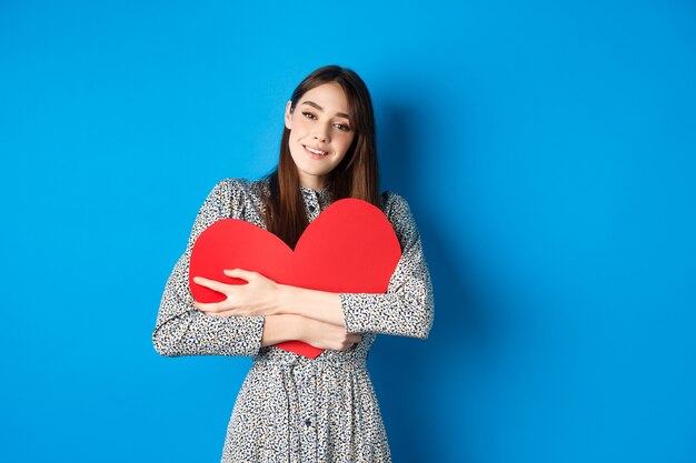 Valentinstag verträumte romantische frau, die großen roten herzausschnitt umarmt und sinnlich in die kamera schaut...