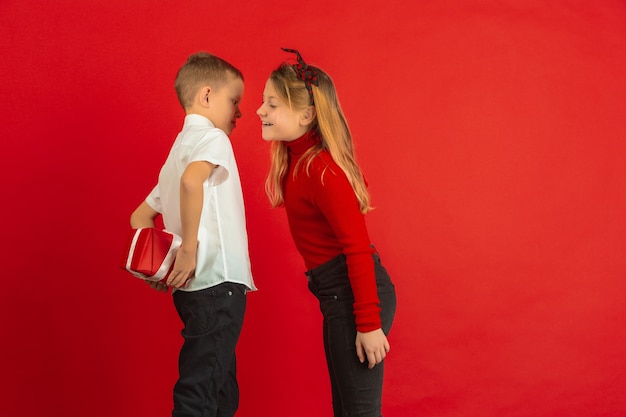 Valentinstagfeier, glückliche, niedliche kaukasische Kinder lokalisiert auf rotem Studio