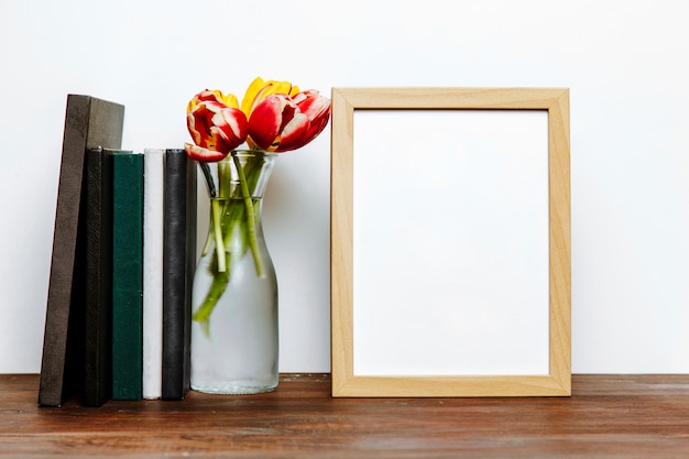 Vase mit Blumen zwischen Büchern und Rahmen