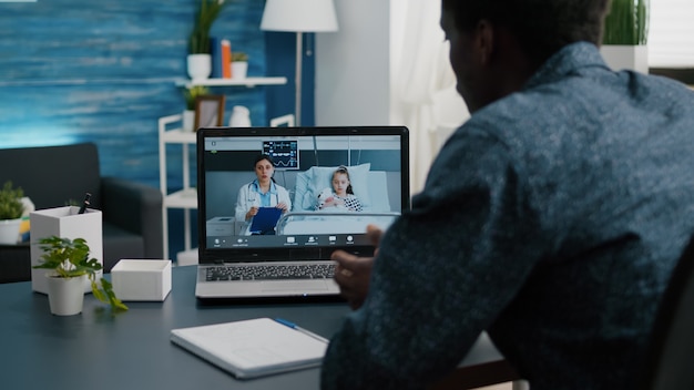 Vater bei Online-Videoanruf über Laptop, im Gespräch mit Arzt aus der Krankenstation