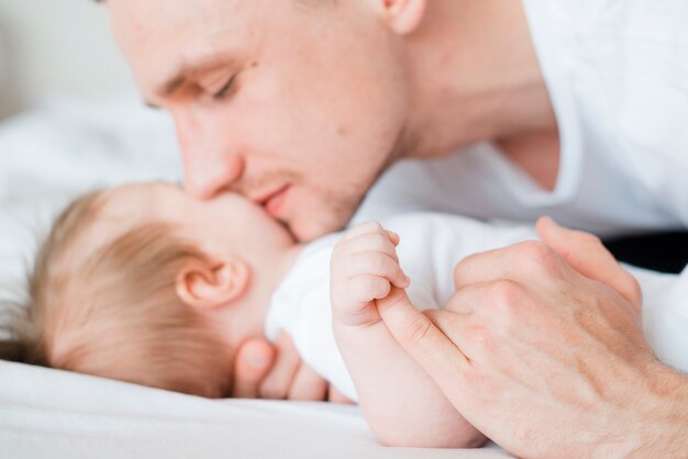 Vater, der Baby in der Stirn im Bett küsst