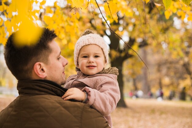 Vater, der Tochter in den Händen im Herbstpark hält