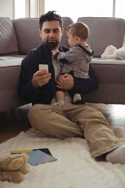 Vater hält sein Baby, während er Handy benutzt