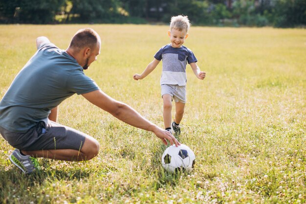 Vater mit dem Sohn, der Fußball am Feld spielt