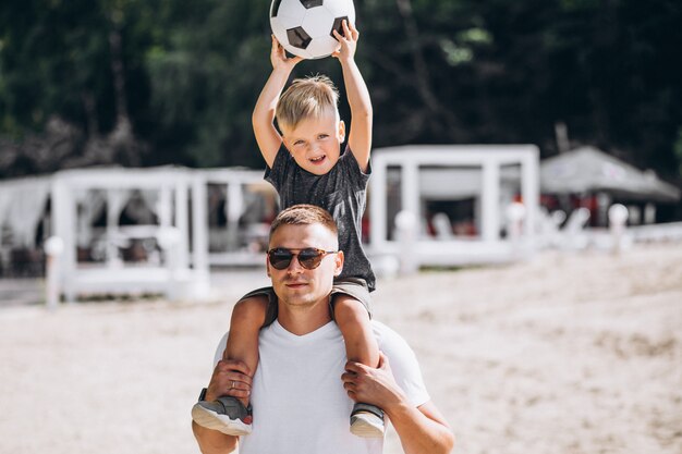 Vater mit dem Sohn, der Fußball am Strand spielt
