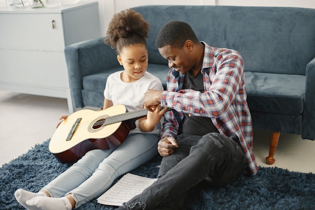 Vater mit Tochter auf der Couch. Mädchen, das eine Gitarre hält. Gitarre lernen.