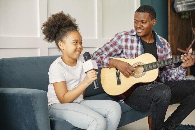 Vater sitzt mit einer Gitarre und Tochter mit einem Mikrofon