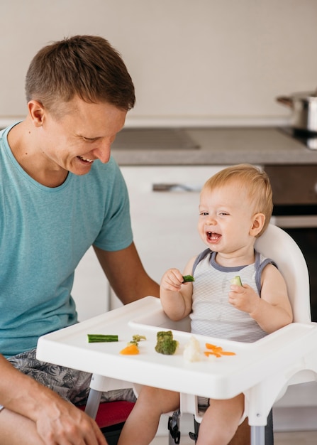 Kostenloses Foto vater und baby im hochstuhl essen