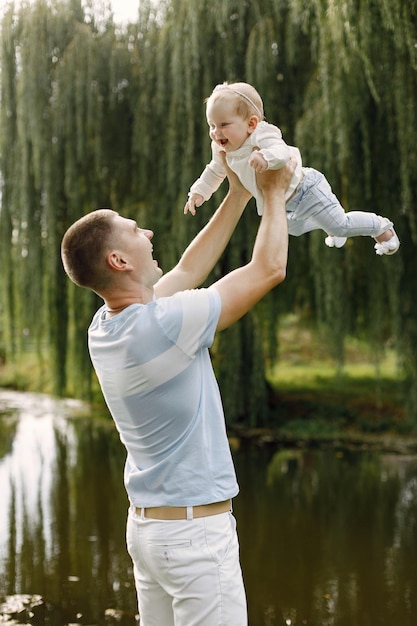 Vater und kleine Tochter stehen im Park und posieren für ein Foto. Familie in weiß-hellblauer Kleidung