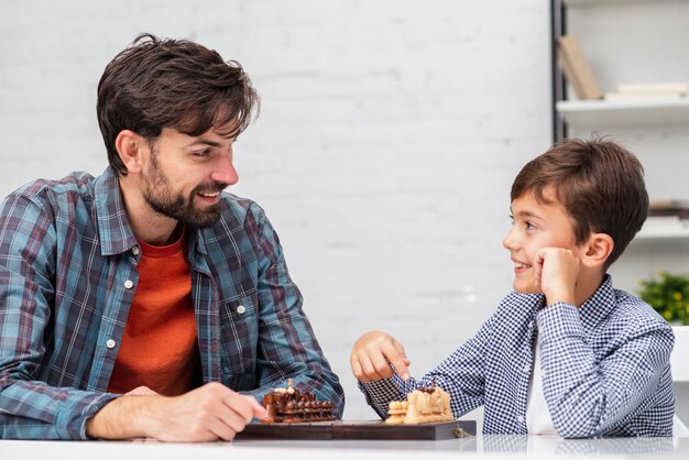 Vater und Sohn, die Schach spielen und einander betrachten