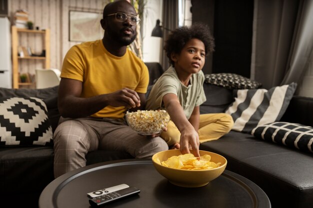 Vater und Sohn essen zusammen Popcorn und Kartoffelchips auf dem Sofa