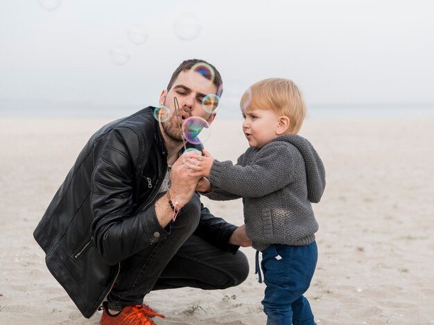 Vater und Sohn machen Seifenblasen am Strand