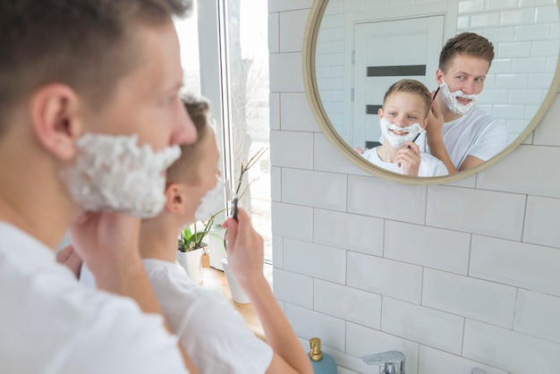 Vater und Sohn rasieren sich im Badezimmerspiegel