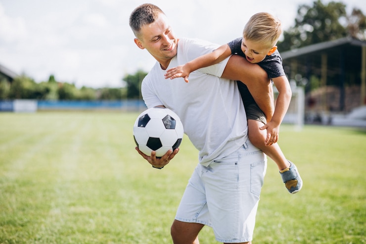 Kostenlose Foto vater und sohn spielen auf dem spielfeld fußball