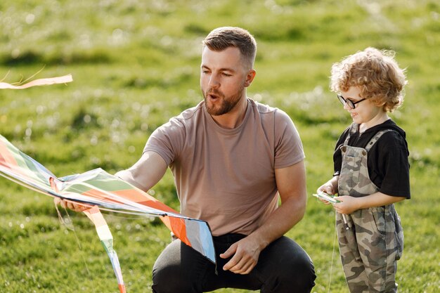 Vater und Sohn spielen mit einem Drachen und haben Spaß im Sommerpark im Freien Curly Kleinkind Junge hat eine Brille