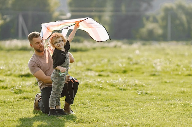 Vater und Sohn spielen mit einem Drachen und haben Spaß im Sommerpark im Freien Curly Kleinkindjunge trägt einen Khaki-Overall