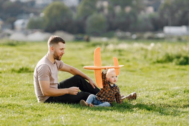 Vater und Sohn spielen mit einem Flugzeugspielzeug und haben Spaß im Sommerpark im Freien Curly Kleinkindjunge in Jeans und kariertem Hemd