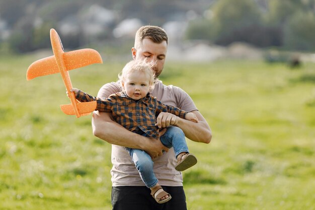 Vater und Sohn spielen mit einem Flugzeugspielzeug und haben Spaß im Sommerpark im Freien Curly Kleinkindjunge in Jeans und kariertem Hemd