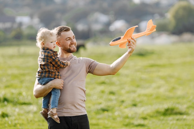 Vater und Sohn spielen mit einem Flugzeugspielzeug und haben Spaß im Sommerpark im Freien Curly Kleinkindjunge in Jeans und kariertem Hemd