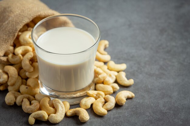 Vegane Cashewmilch im Glas mit Cashewkernen auf dunklem Hintergrund