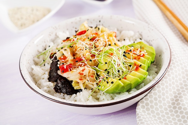 Veganer Salat mit Reis, eingelegtem Kimchi-Kohl, Avocado, Nori und Sesam auf Schüssel.
