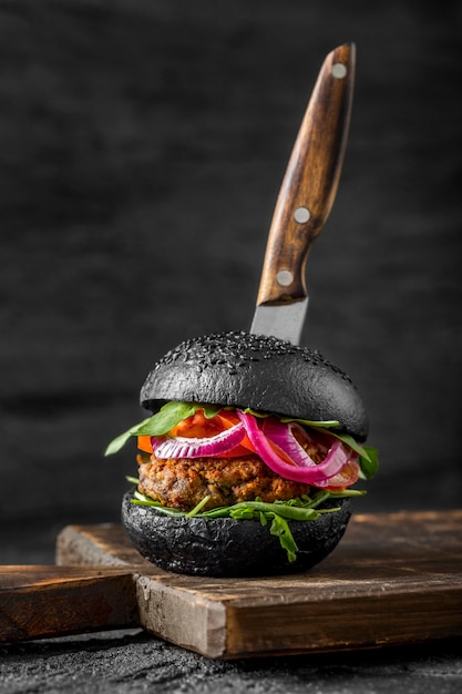 Veggie-Burger von vorne mit schwarzen Brötchen auf Schneidebrett mit Messer