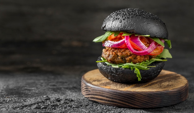 Veggie-Burger von vorne mit schwarzen Brötchen auf Schneidebrett