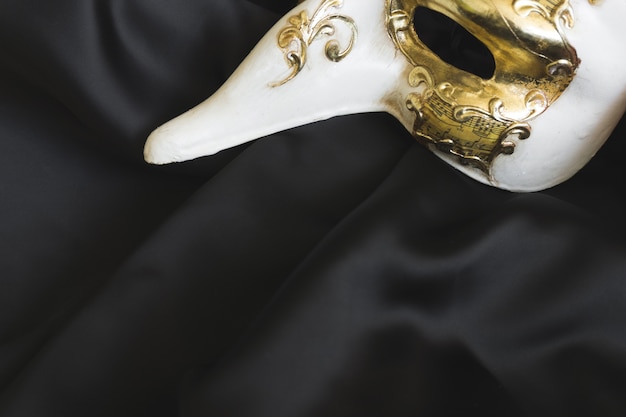 Venezianische Maske mit einer langen Nase auf einem dunklen Tuch