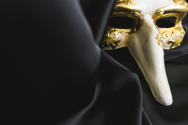 Venezianische Maske mit einer langen Nase auf einem dunklen Tuch