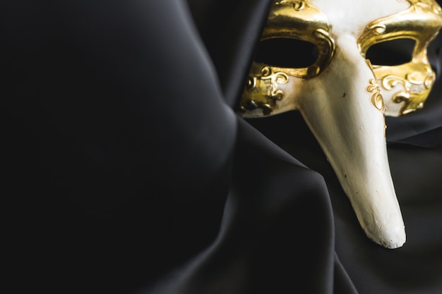 Venezianische Maske mit einer langen Nase auf einem dunklen Tuch