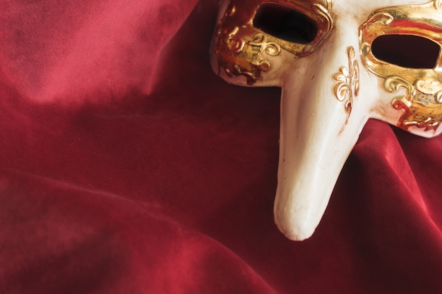 Venezianische Maske mit einer langen Nase auf einem roten Stoff