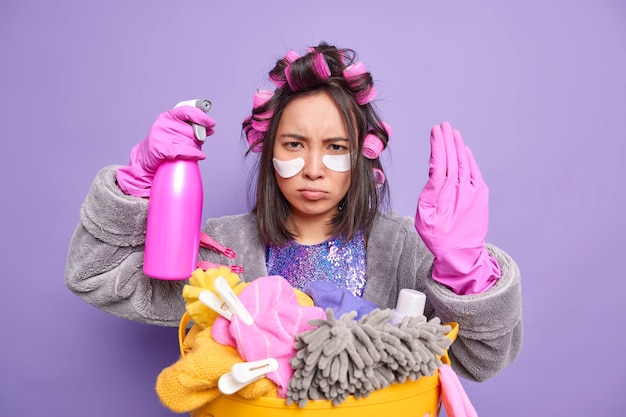 Verärgerte asiatische Frau macht Stop-Geste bittet zu halten verbietet Aktion trägt Hausmantel Gummihandschuhe, die mit Reinigung beschäftigt sind, und Waschen macht Frisur-Posen drinnen. Housekeeping-Konzept