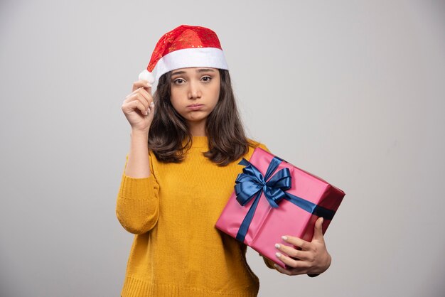Verärgerte Frau im roten Hut des Weihnachtsmanns mit Weihnachtsgeschenk.