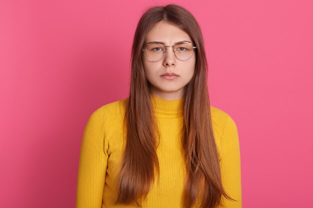 Verärgerte Frau mit langen glatten Haaren, lässigem Outfit und Brille, mit traurigem Gesichtsausdruck, sieht enttäuscht aus