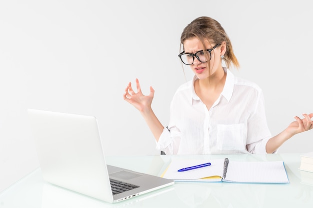 Verärgerte junge Frau, die am Schreibtisch lokalisiert über Hintergrund schreit