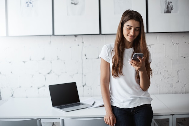 Verärgerte junge Frau, die Smartphone verwendet, um zu überprüfen, ob jemand ihre Fotos mag. Verschleppung ihres Prüfungsstudiums.