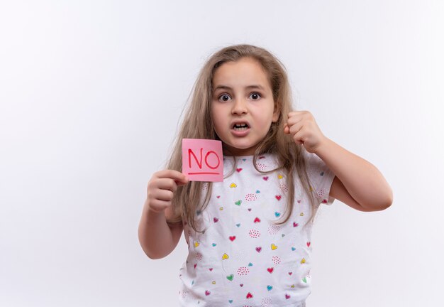 Verärgerte kleine Schulfrau, die weißes T-Shirt hält Papiermarke auf isolierter weißer Wand hält