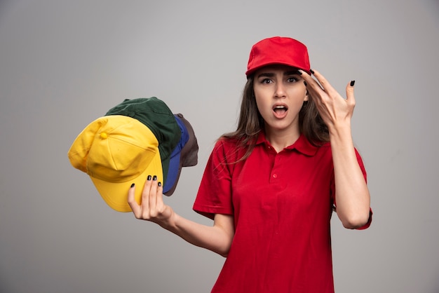 Verärgerte Lieferfrau in der roten Uniform, die bunte Kappen hält.