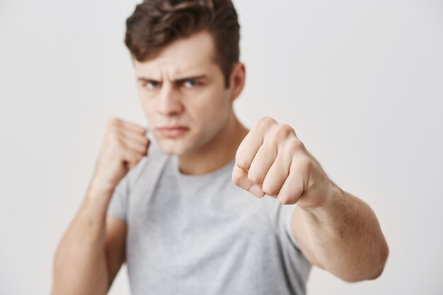 Verärgerter, aggressiver junger kaukasischer Mann, der in einer Verteidigungsposition steht, die Fäuste geballt hält, einen selbstbewussten Blick hat, bereit ist, sich zu verteidigen und für seine Rechte eintritt