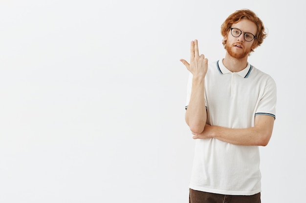 Kostenloses Foto verärgerter oder gelangweilter bärtiger rotschopf, der mit brille gegen die weiße wand posiert