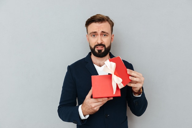 Verärgerter trauriger Mann im Anzug, der Geschenk hält und Kamera lokalisiert